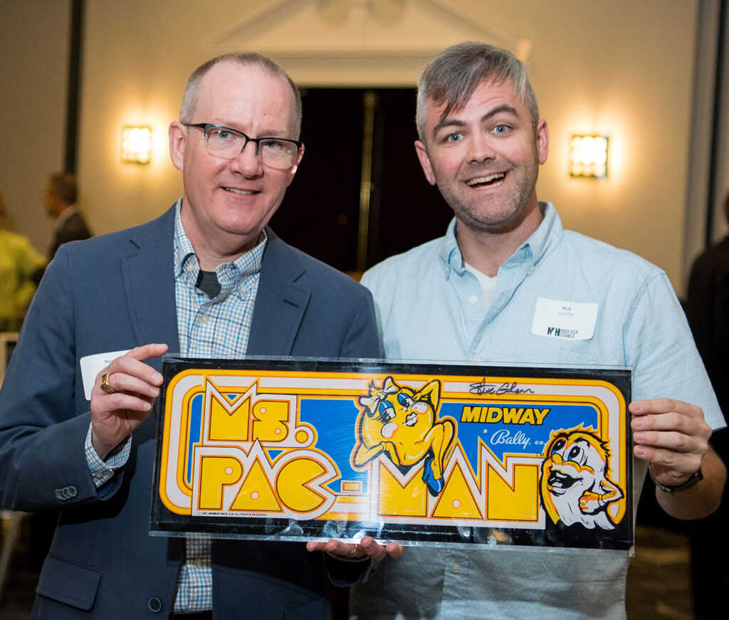 Two older men holding a Ms. Pac-Man sign